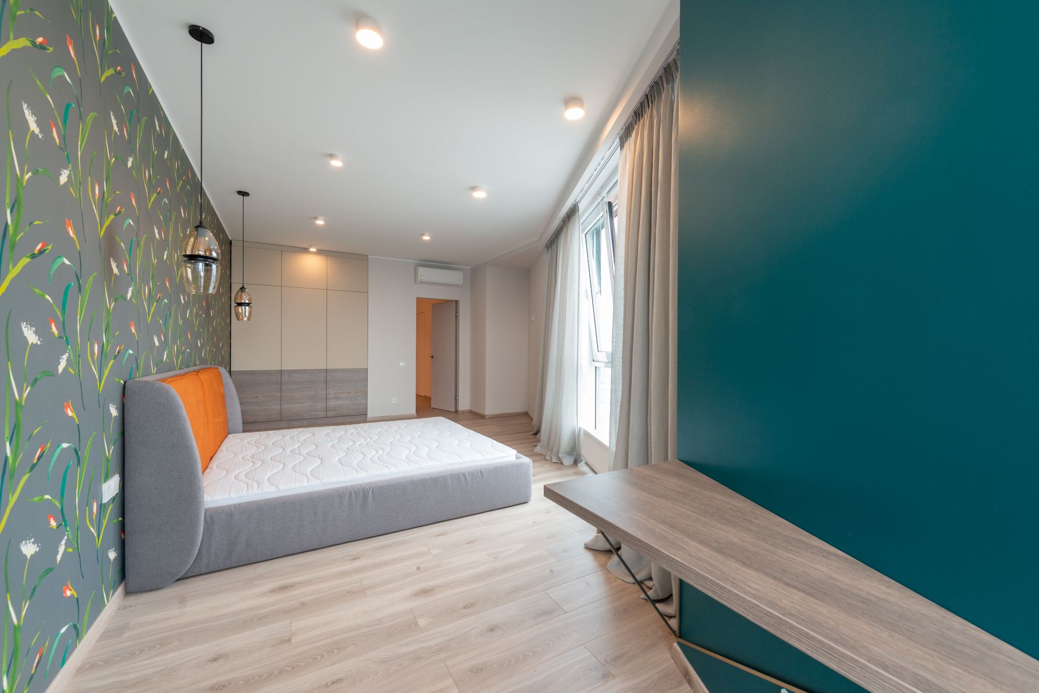 Vibrant floral wallpaper behind a bed and decorative hanging lamps in a finished bedroom