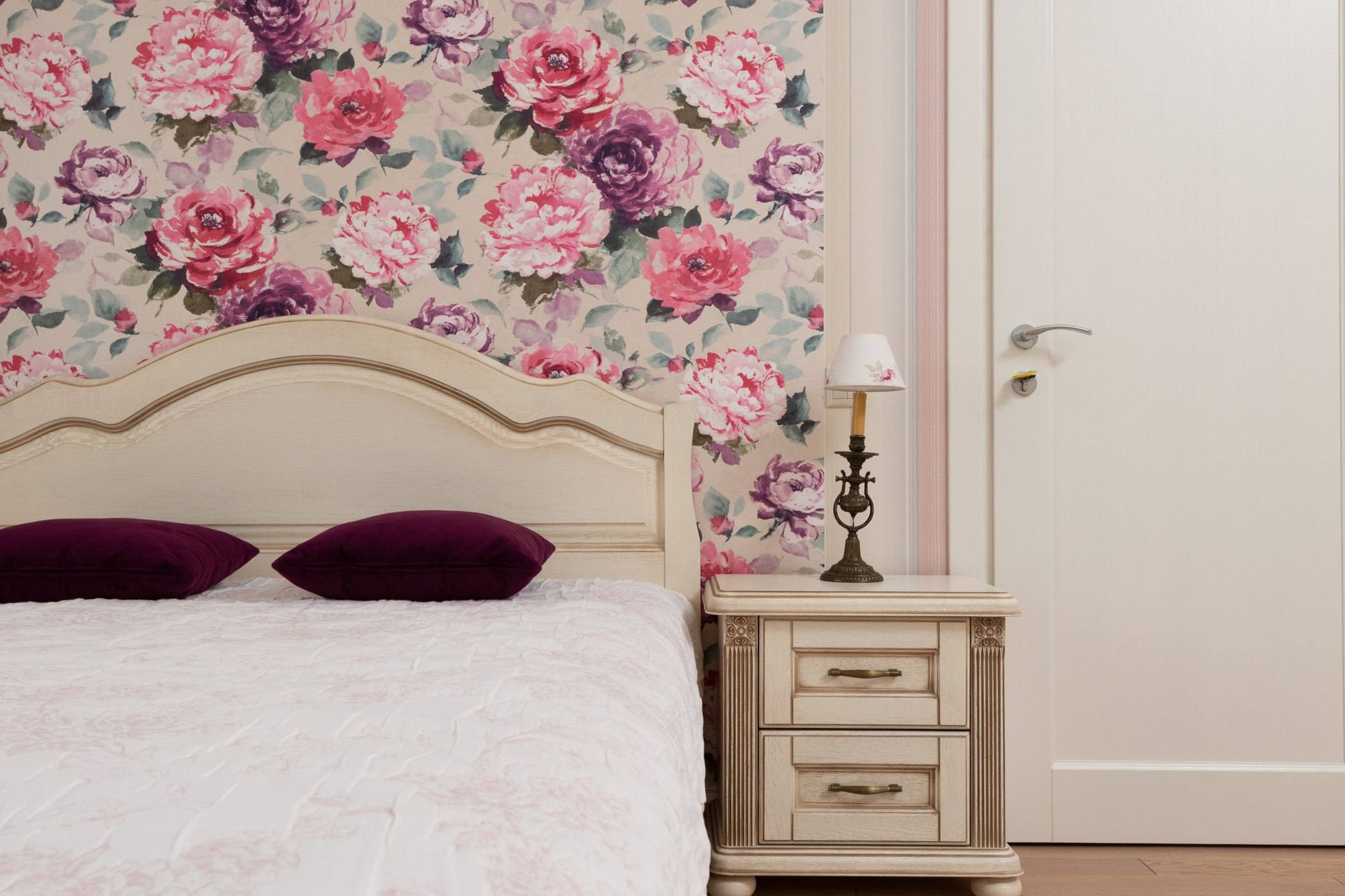Large floral wallpaper installed behind a bed and classic bedside table