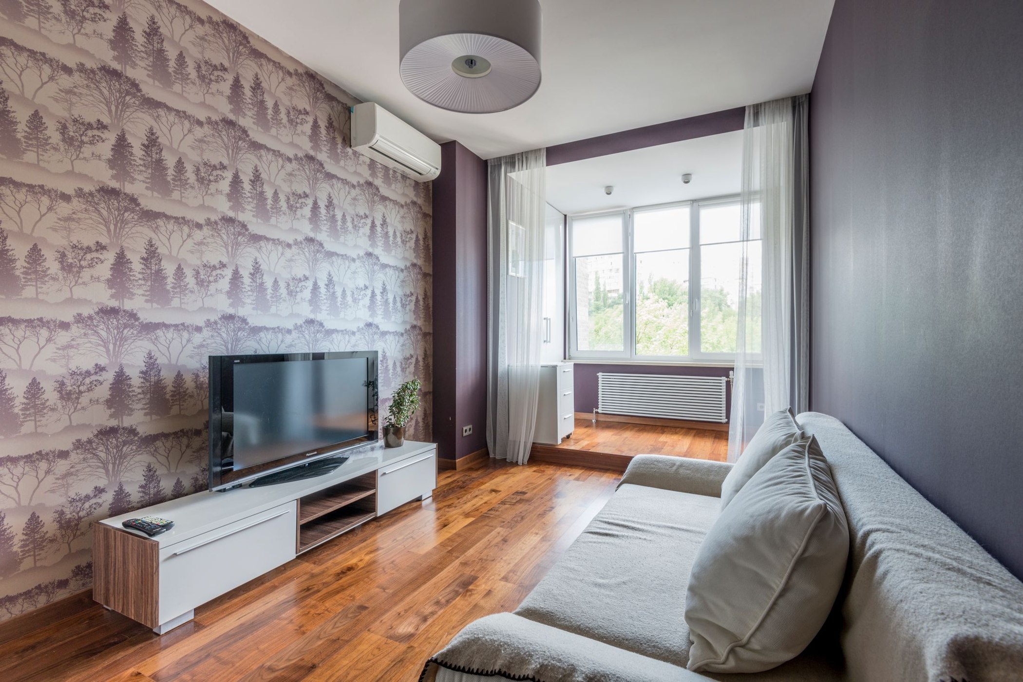 Plum woodland wallpaper feature wall in a contemporary living room with a sofa and television